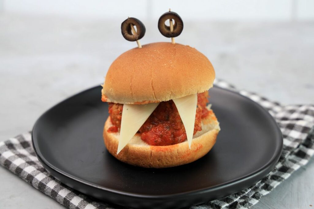 Monster meatball slider with cheese as teeth and meatball in the middle. Toothpicks with black olives as eyes.