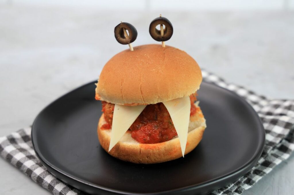 Monster meatball slider with cheese as teeth and meatball in the middle. Toothpicks with black olives as eyes.