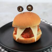 Monster meatball slider with cheese as teeth and meatball in the middle. Toothpicks with black olives as eyes.