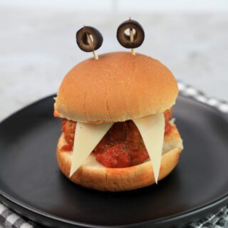 Monster meatball slider with cheese as teeth and meatball in the middle. Toothpicks with black olives as eyes.