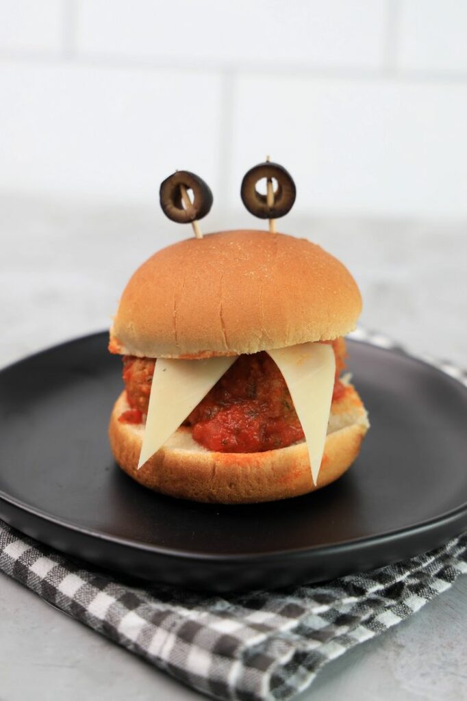 Monster meatball slider with cheese as teeth and meatball in the middle. Toothpicks with black olives as eyes.