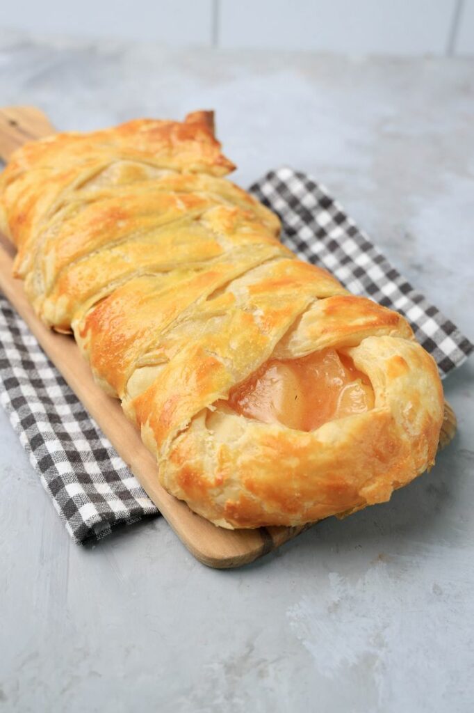 Apple Pie Cream Cheese Braid on a wood board on a plaid napkin.