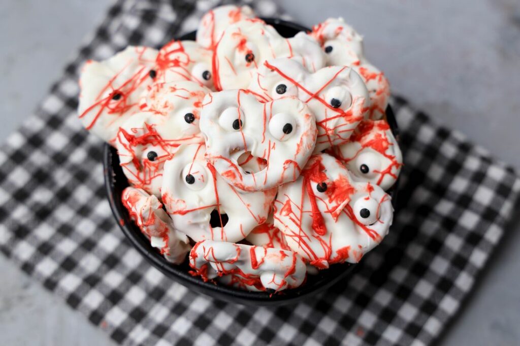 Bloody ghost pretzels in a black bowl with a gray plaid napkin on a faux concrete back drop.