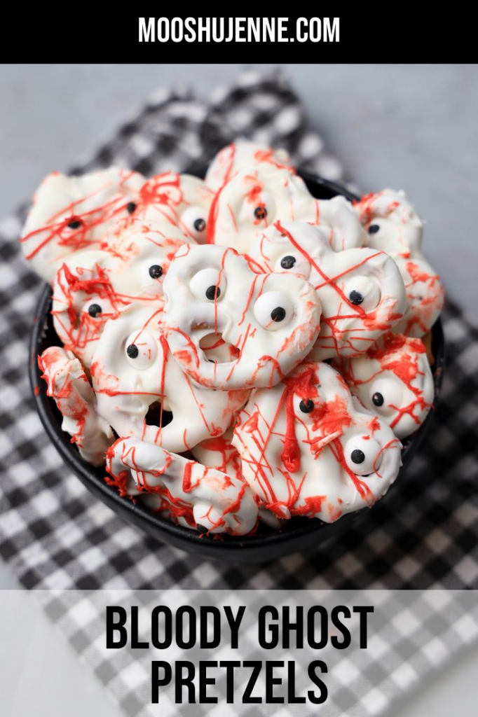 Bloody ghost pretzels that are white with red blood splatter in a black bowl.