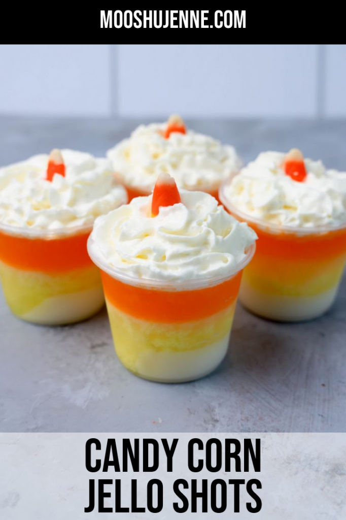 Candy corn layered jello shots topped with whipped topping and a piece of candy corn on a faux concrete backdrop