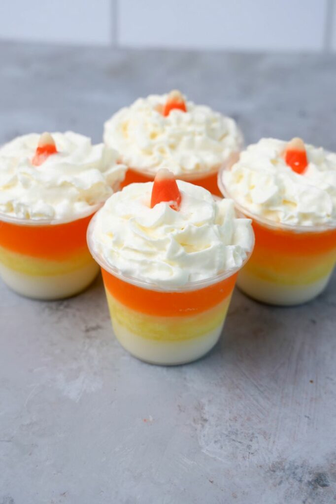 Candy corn layered jello shots topped with whipped topping and a piece of candy corn on a faux concrete backdrop