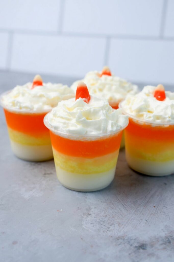 Candy corn layered jello shots topped with whipped topping and a piece of candy corn on a faux concrete backdrop