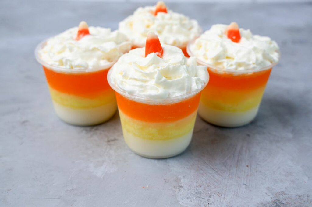 Candy corn layered jello shots topped with whipped topping and a piece of candy corn on a faux concrete backdrop