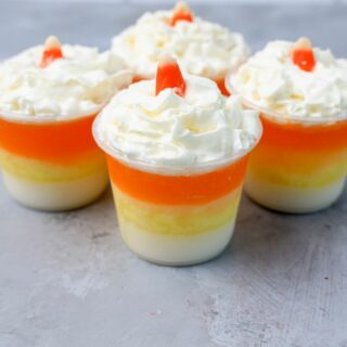 Candy corn layered jello shots topped with whipped topping and a piece of candy corn on a faux concrete backdrop