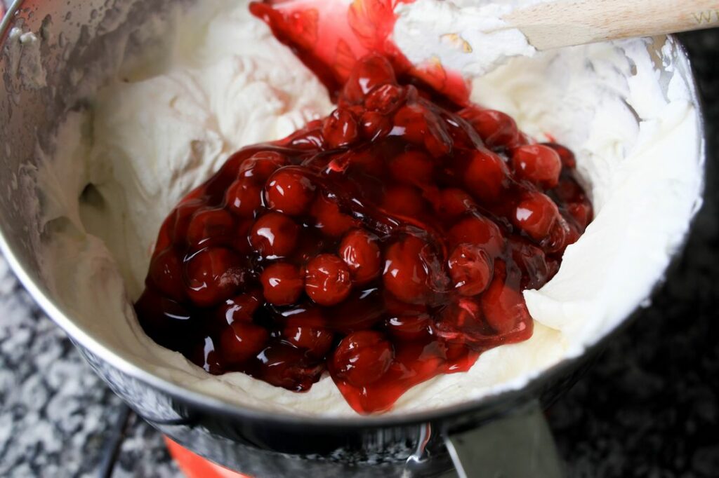 Cream mixture and cherry pie filling in the stand mixer bowl.