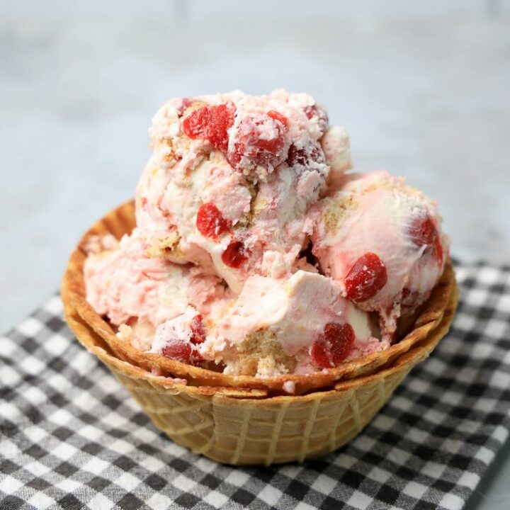 Cherry Pie Ice Cream in a waffle cone bowl with a gray plaid napkin on a faux concrete backdrop.
