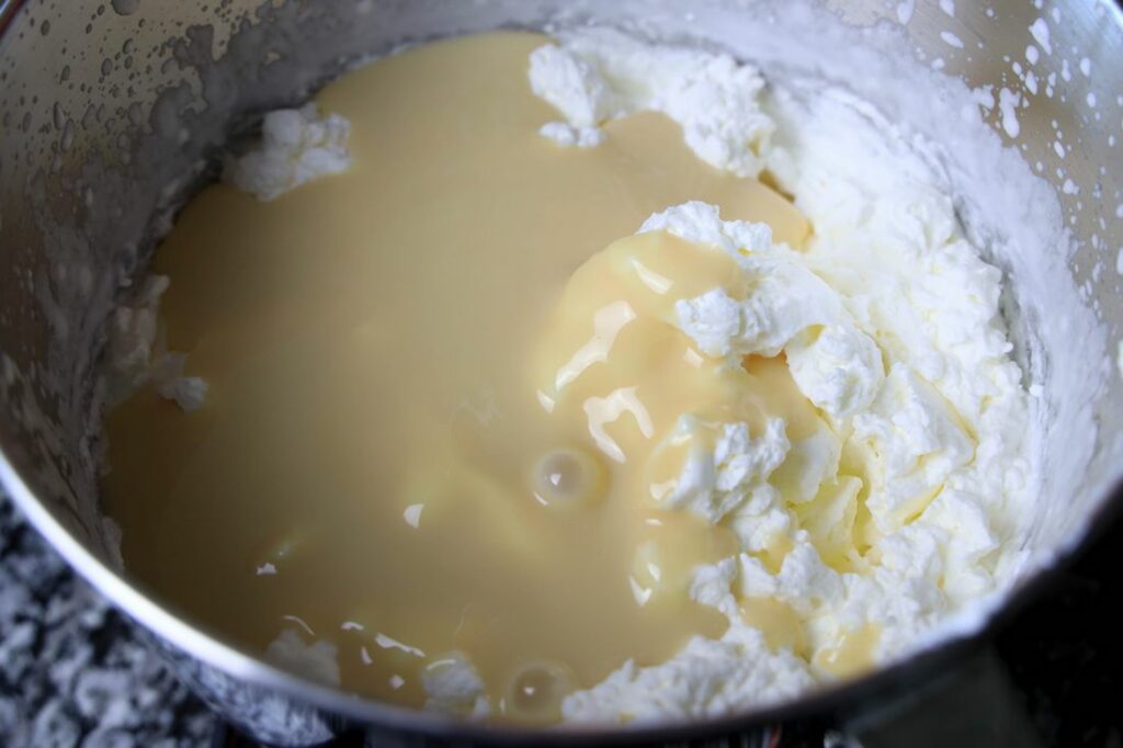 Whipped topping and sweetened condensed milk in the stand mixer bowl.