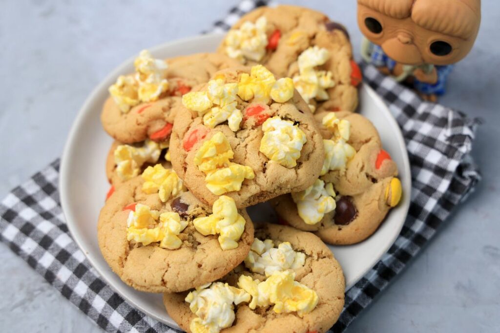 Peanut butter cookies with reese's pieces and popcorn on a white plate with a gray plaid napkin. ET funko pop in background