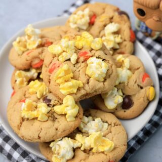 Peanut butter cookies with reese's pieces and popcorn on a white plate with a gray plaid napkin. ET funko pop in background