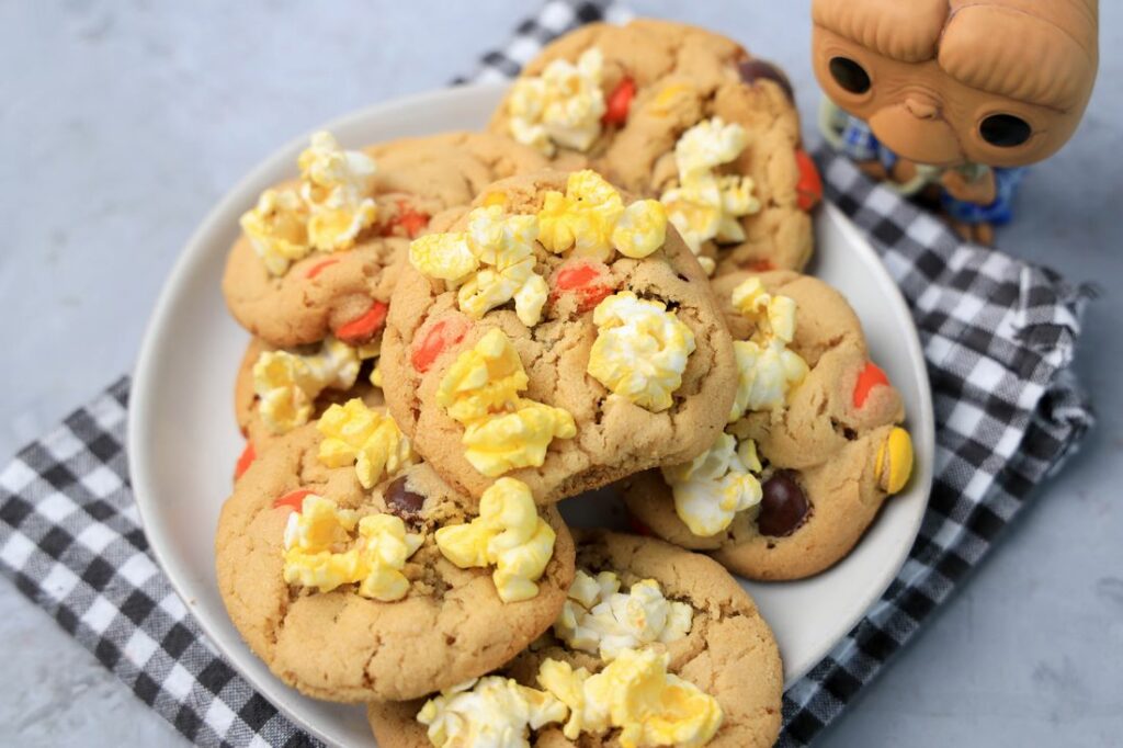 Peanut butter cookies with reese's pieces and popcorn on a white plate with a gray plaid napkin. ET funko pop in background.