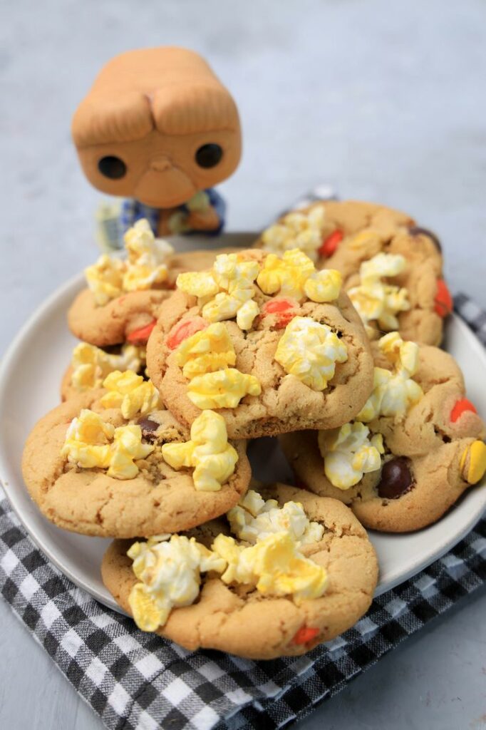 Peanut butter cookies with reese's pieces and popcorn on a white plate with a gray plaid napkin. ET funko pop in background