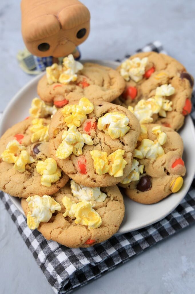 Peanut butter cookies with reese's pieces and popcorn on a white plate with a gray plaid napkin. ET funko pop in background