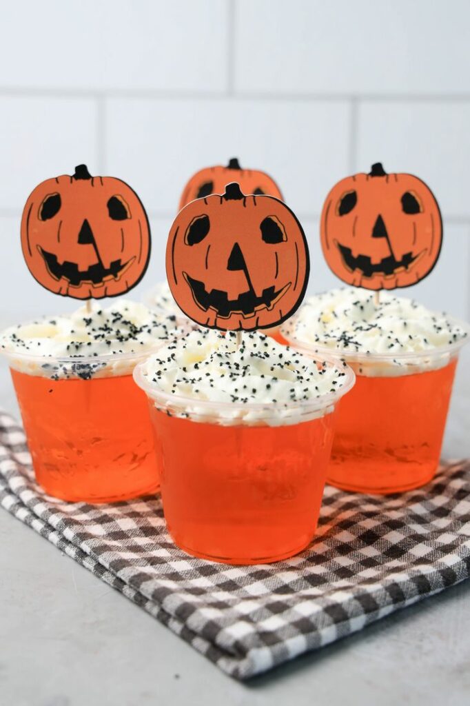 Halloween Movie Pumpkin Jello Shots that are orange topped with whipped topping and black sprinkles. With the 1978 Halloween Movie Pumpkin Topper.