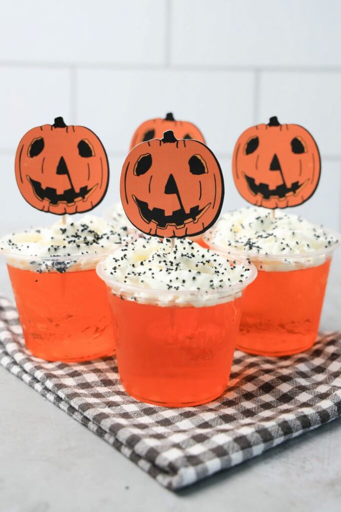 Halloween Movie Pumpkin Jello Shots that are orange topped with whipped topping and black sprinkles. With the 1978 Halloween Movie Pumpkin Topper.