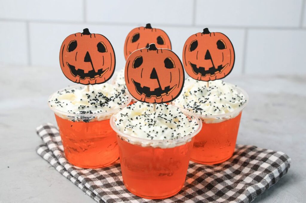 Halloween Movie Pumpkin Jello Shots that are orange topped with whipped topping and black sprinkles. With the 1978 Halloween Movie Pumpkin Topper.