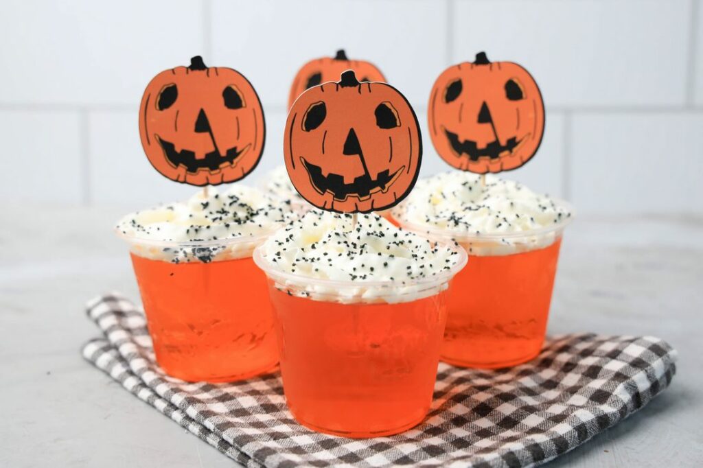 Halloween Movie Pumpkin Jello Shots that are orange topped with whipped topping and black sprinkles. With the 1978 Halloween Movie Pumpkin Topper.