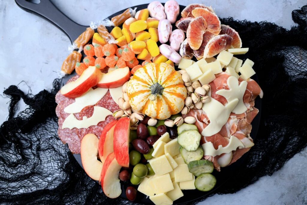 Black board with meats, cheese, a pumpkin, halloween candies, pickles, and olives.