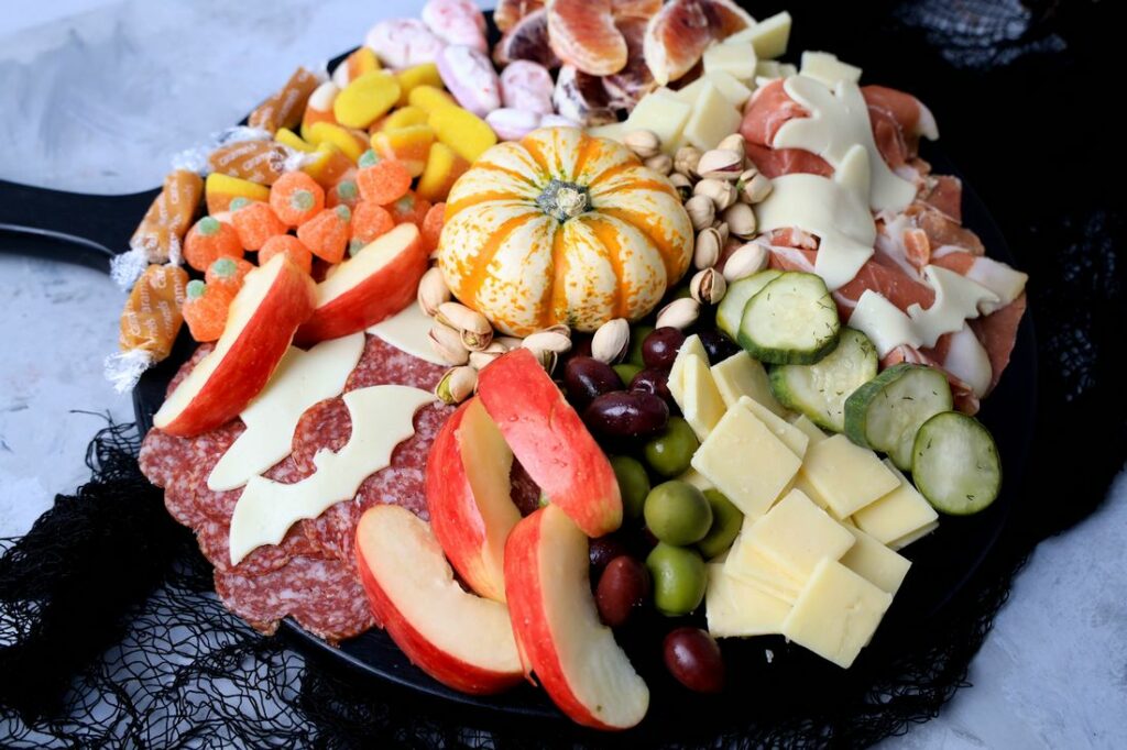 Black board with meats, cheese, a pumpkin, halloween candies, pickles, and olives.