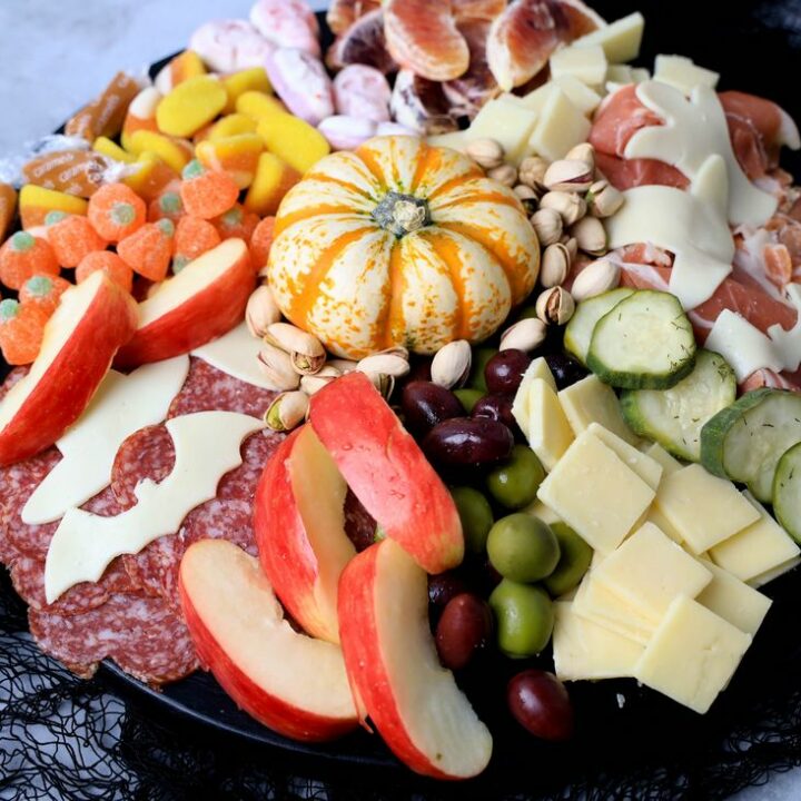 Black board with meats, cheese, a pumpkin, halloween candies, pickles, and olives.
