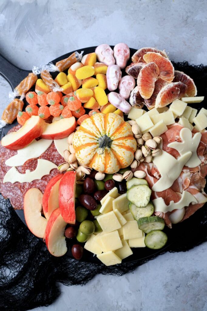 Black board with meats, cheese, a pumpkin, halloween candies, pickles, and olives.