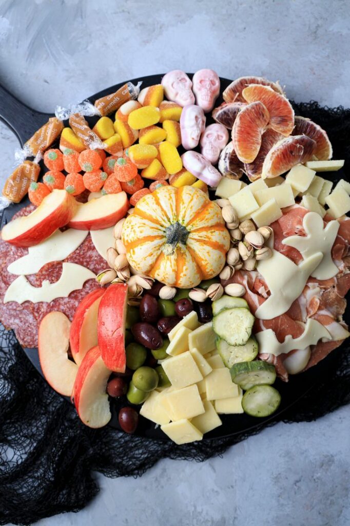 Black board with meats, cheese, a pumpkin, halloween candies, pickles, and olives.