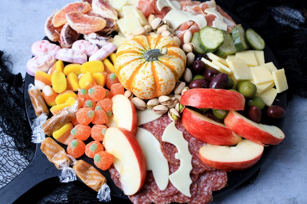 Black board with meats, cheese, a pumpkin, halloween candies, pickles, and olives.