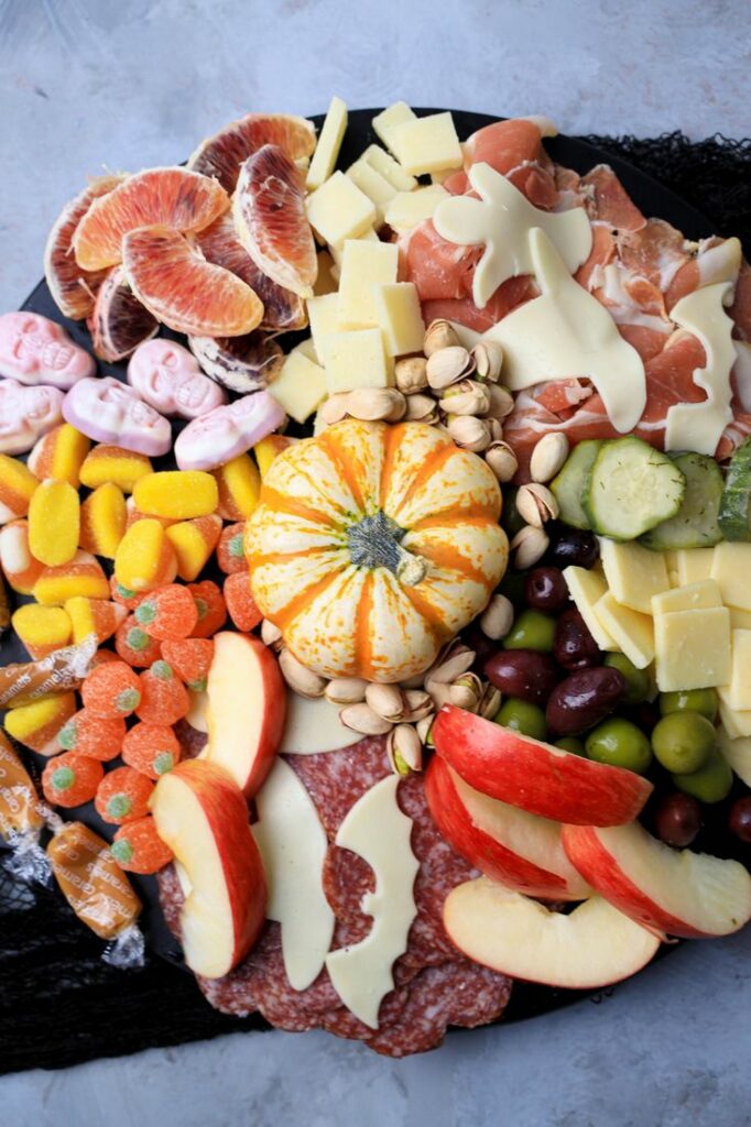 Black board with meats, cheese, a pumpkin, halloween candies, pickles, and olives.