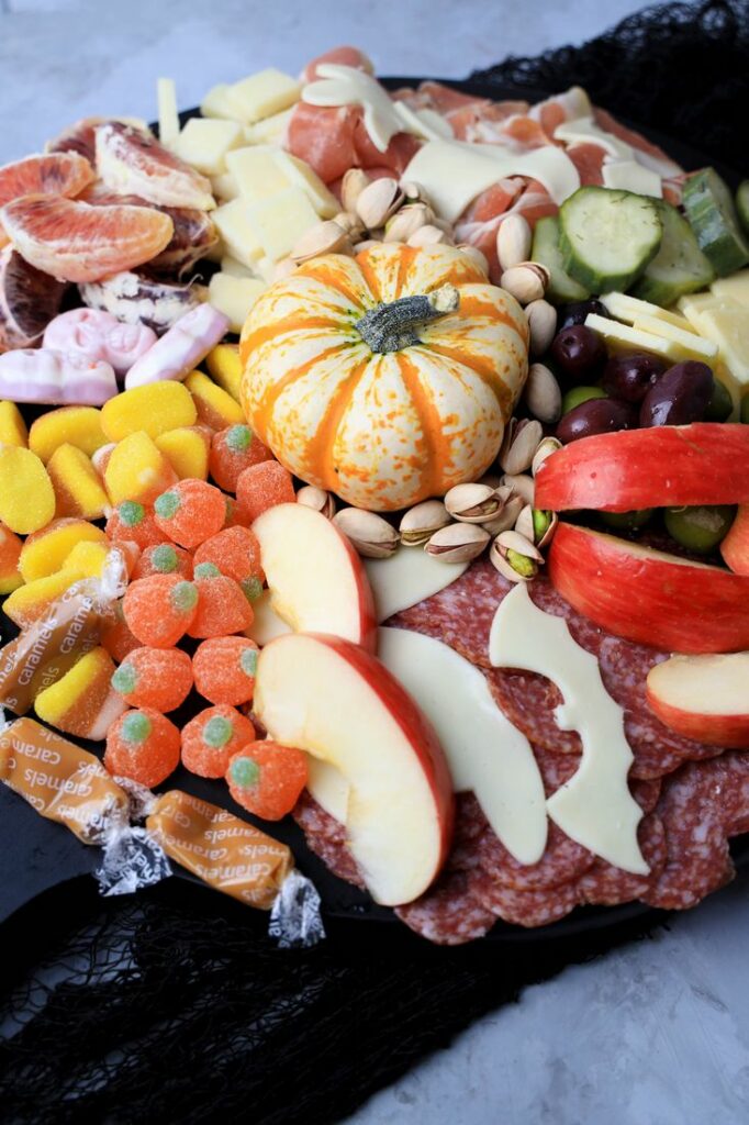 Black board with meats, cheese, a pumpkin, halloween candies, pickles, and olives.