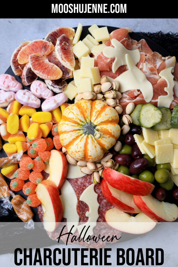 Black board with meats, cheese, a pumpkin, halloween candies, pickles, and olives.