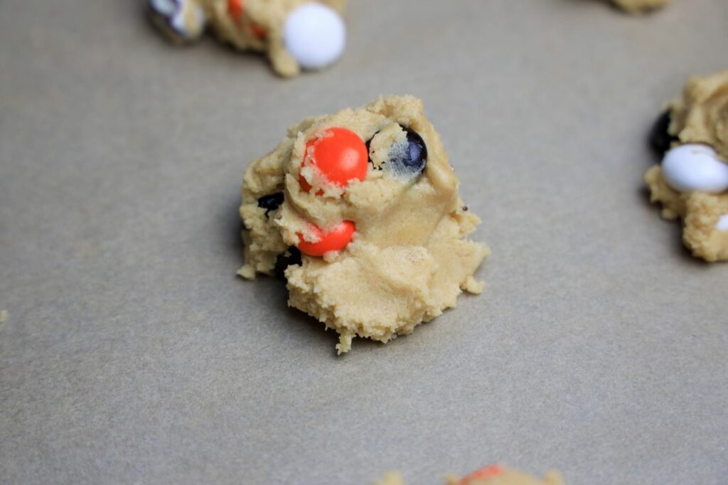 Scoop of cookie dough on a parchment lined baking sheet.