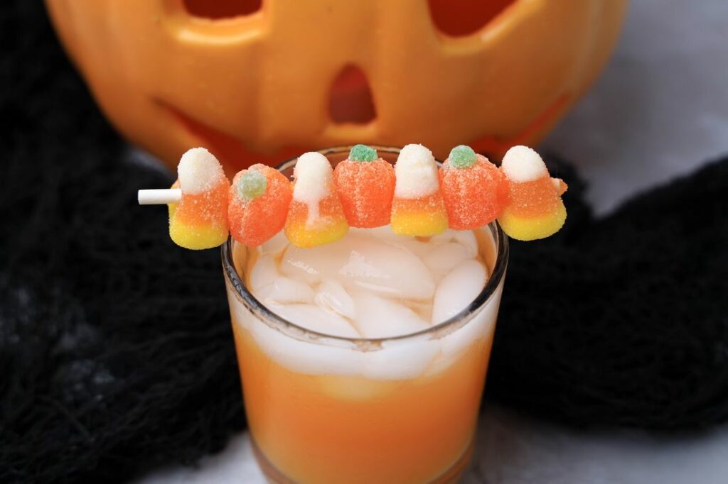 Halloween Michael Myers Cocktail with orange juice and orange soda. Topped with candy corn and pumpkin gummies. With the original myer's pumpkin in the back.