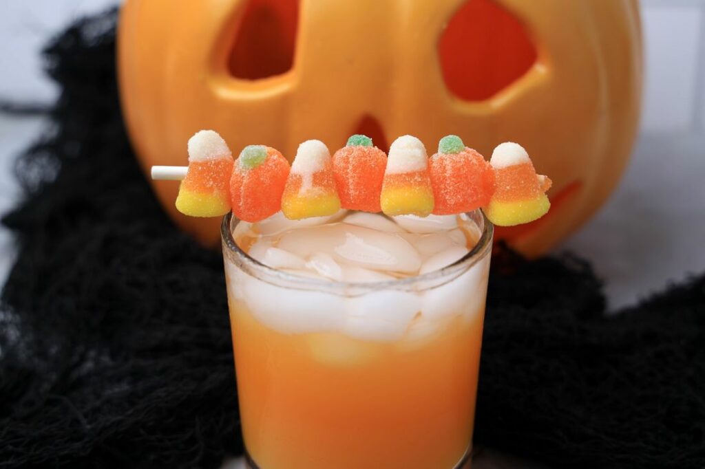 Halloween Michael Myers Cocktail with orange juice and orange soda. Topped with candy corn and pumpkin gummies. With the original myer's pumpkin in the back.