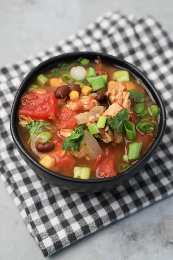 Instant Pot Baja Chicken Soup in a black bowl on a gray plaid napkin with concrete backdrop.