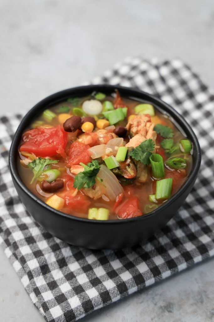 Instant Pot Baja Chicken Soup in a black bowl on a gray plaid napkin with concrete backdrop.