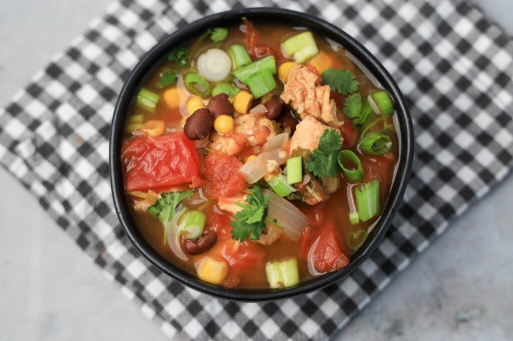 Instant Pot Baja Chicken Soup in a black bowl on a gray plaid napkin with concrete backdrop.