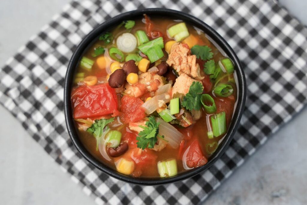 Instant Pot Baja Chicken Soup in a black bowl on a gray plaid napkin with concrete backdrop.