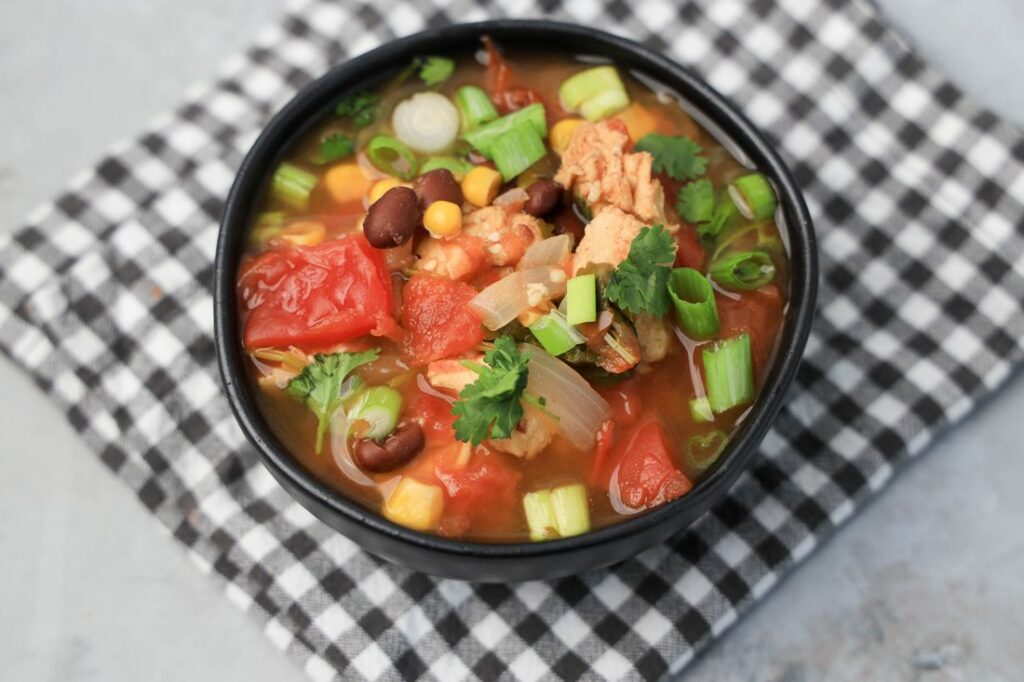 Instant Pot Baja Chicken Soup in a black bowl on a gray plaid napkin with concrete backdrop.