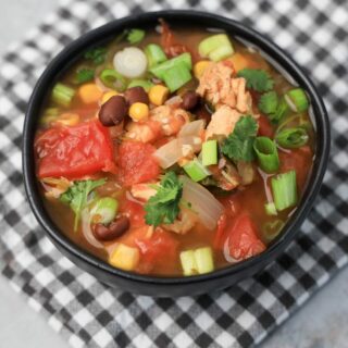 Instant Pot Baja Chicken Soup in a black bowl on a gray plaid napkin with concrete backdrop.