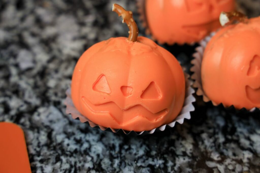 Jack O'Lantern hot chocolate bomb in a cupcake liner with a pretzel top.