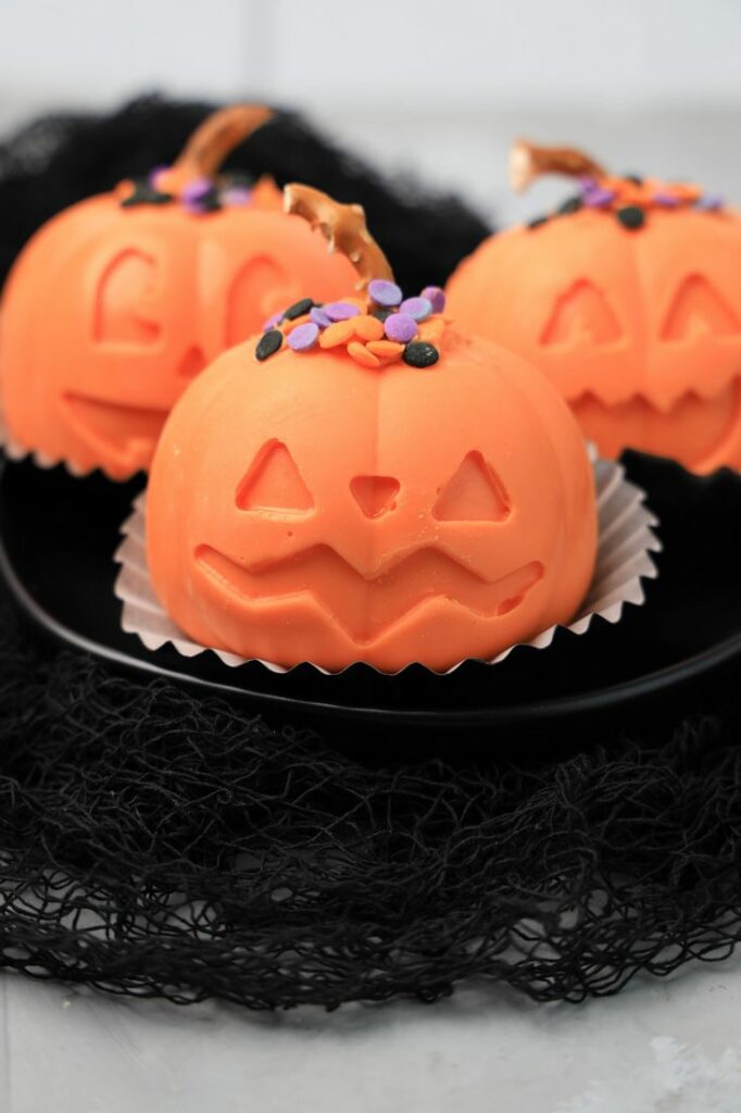 Jack O' Lantern Hot Chocolate bomb on a black plate with black mesh.