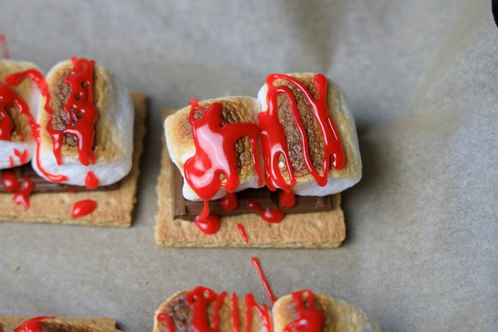 Red cookie icing on top of toasted marshmallows on a bed of chocolate and graham crackers.