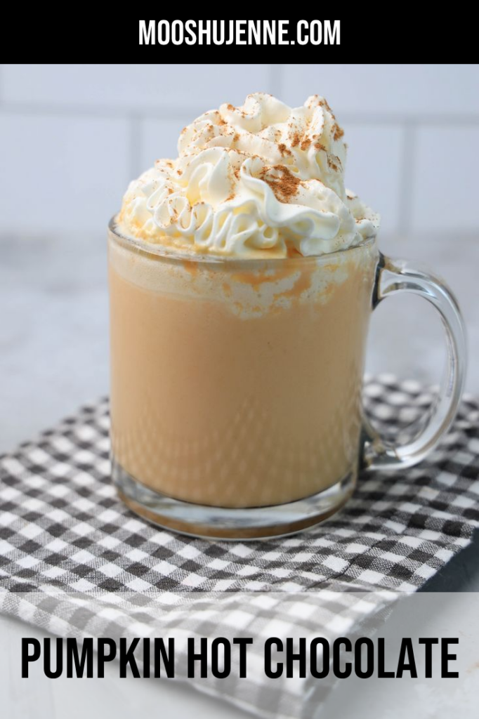 Pumpkin Hot Chocolate in a clear glass on a plaid napkin on a concrete backdrop