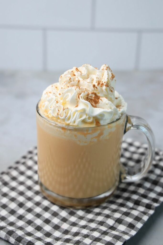 Pumpkin Hot Chocolate in a clear glass on a plaid napkin on a concrete backdrop