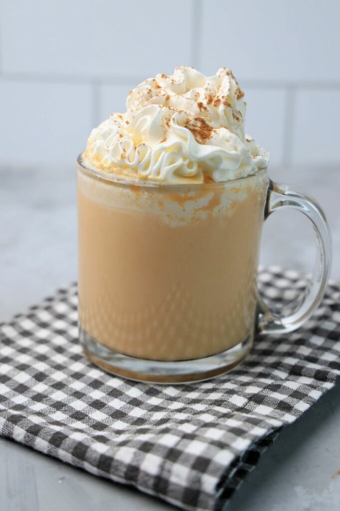 Pumpkin Hot Chocolate in a clear glass on a plaid napkin on a concrete backdrop