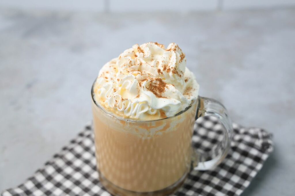Pumpkin Hot Chocolate in a clear glass on a plaid napkin on a concrete backdrop